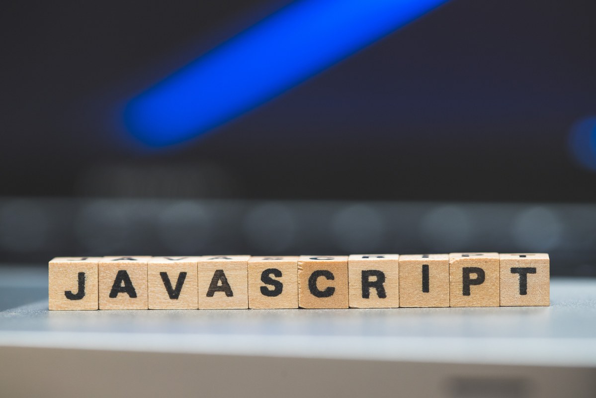 Wooden cubes with letters “JAVASCRIPT” lying on a laptop.