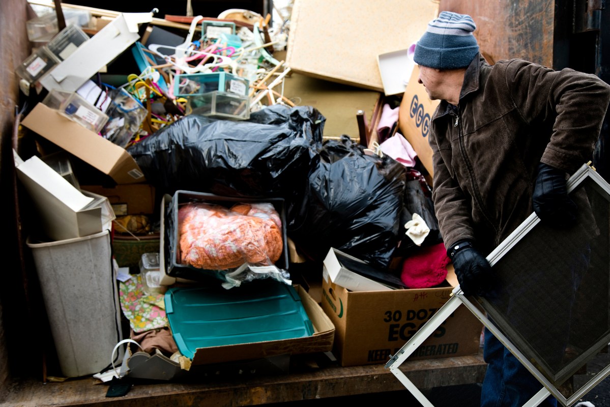 Workman loading junk in dumpster.