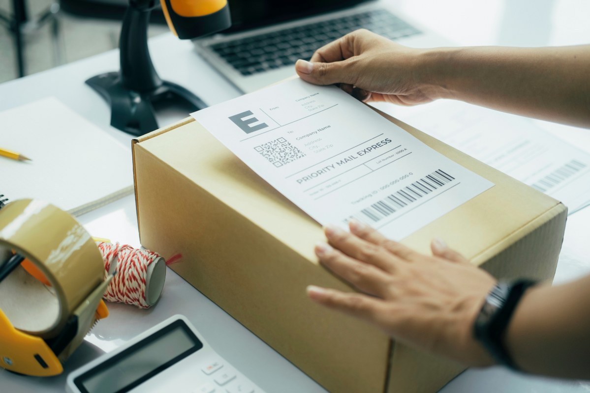 Young business owner putting priority shipping label on parcel.