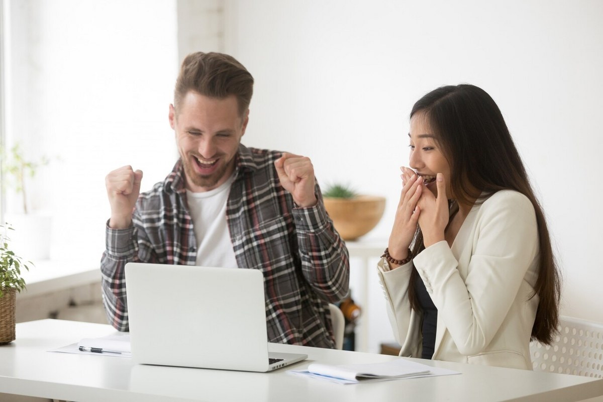 A happy couple sits together in front of their laptop.