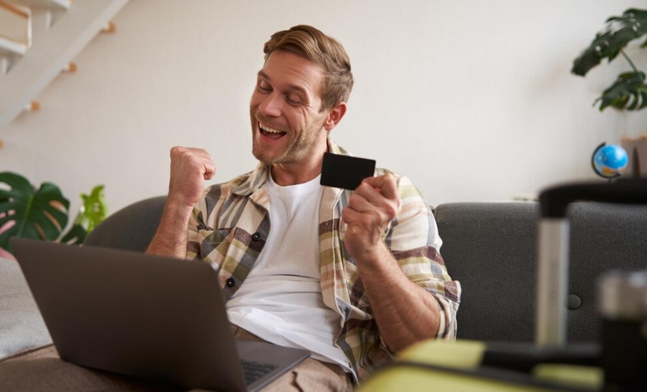 A happy man holding his credit card while looking at a laptop.