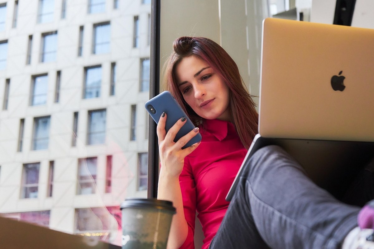 A woman holding a computer while using her phone.