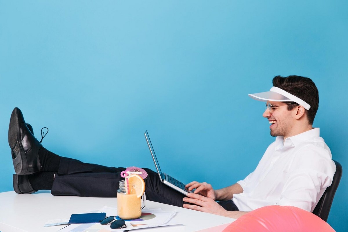 Cheerful guy in cap works in laptop and laughs.