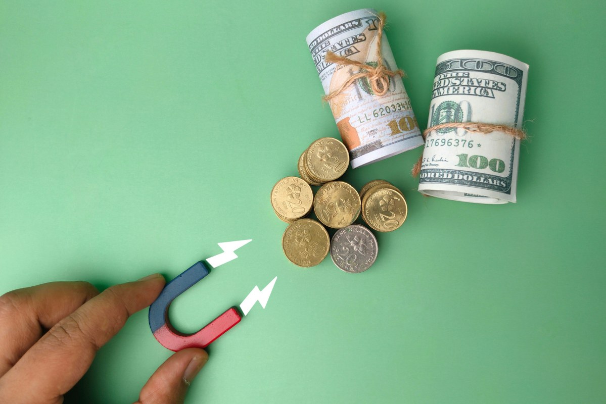 Hand holding a magnet attracts money using magnet.