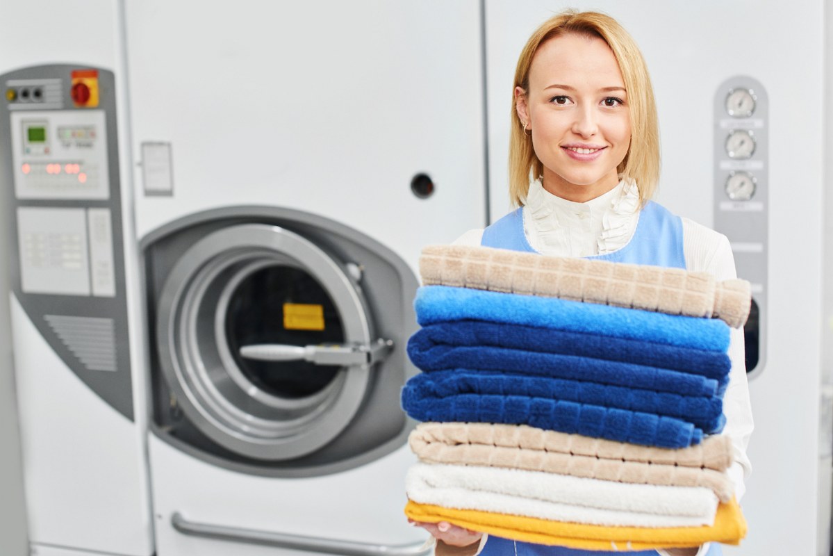 Laundry shop worker smiles while holding folded towels.
