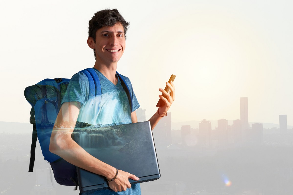Male Digital Nomad looking at camera, holding a phone and a laptop.
