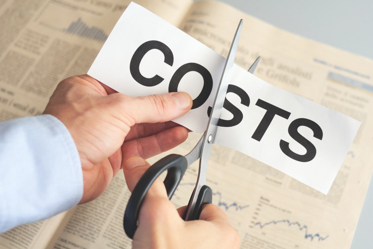 Male hands cutting paper with word COSTS.
