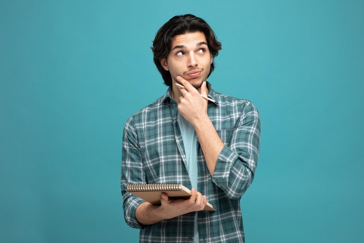 Man holding pencil and note pad keeping a hand on chin.