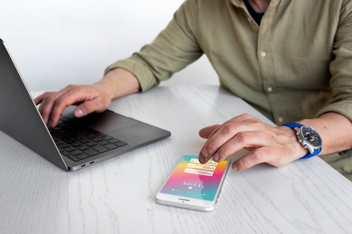 Man is sitting in front of a laptop and a phone.