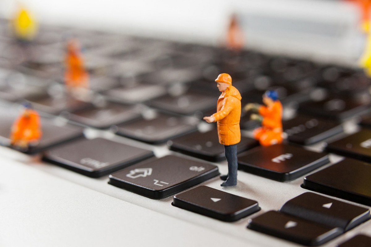 Miniature workmen at laptop keyboard.