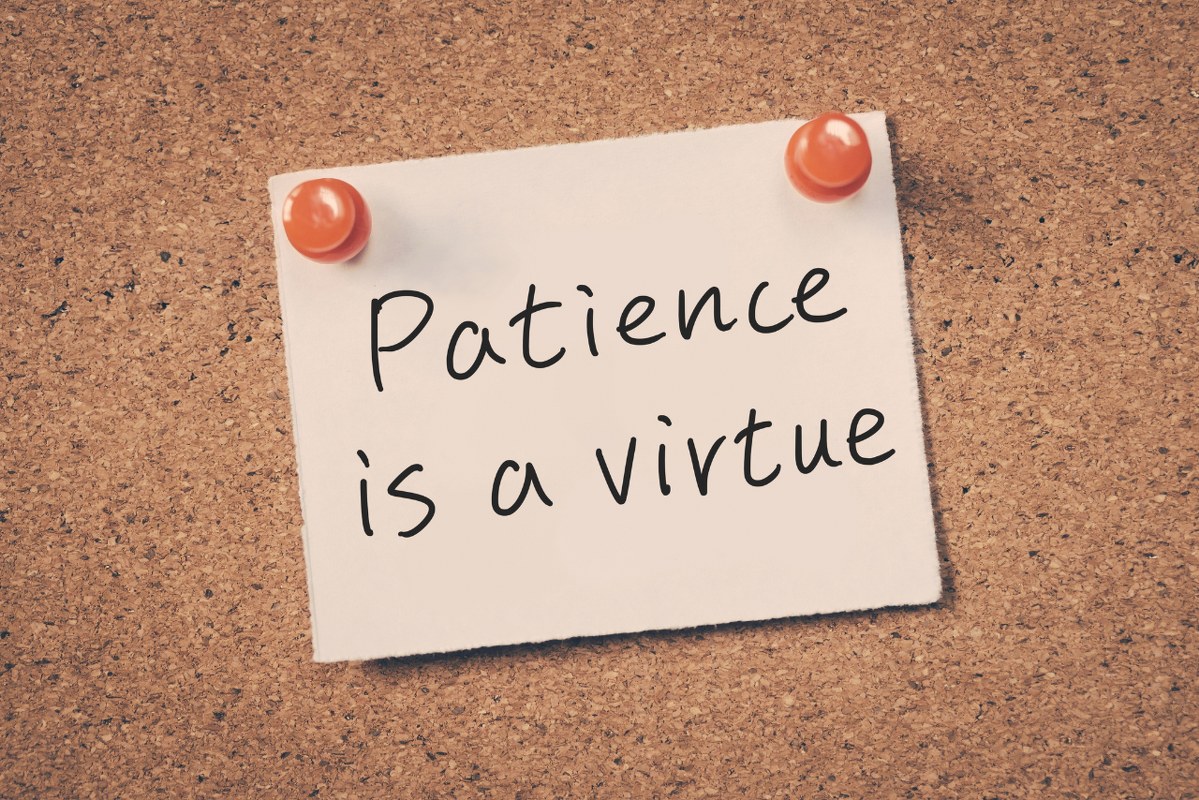 Patience is a virtue reminder note on a cork board.
