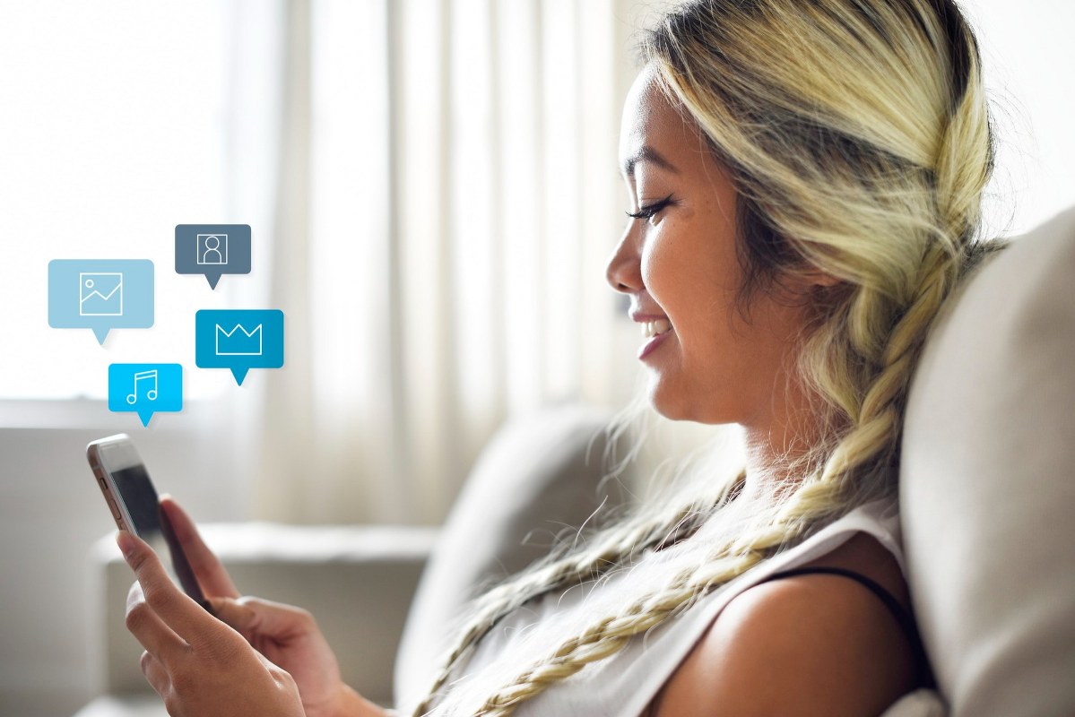 Smiling woman using a smartphone on a couch.