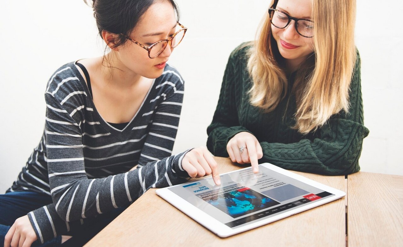 Two women are collaborating on a project using their tablets.