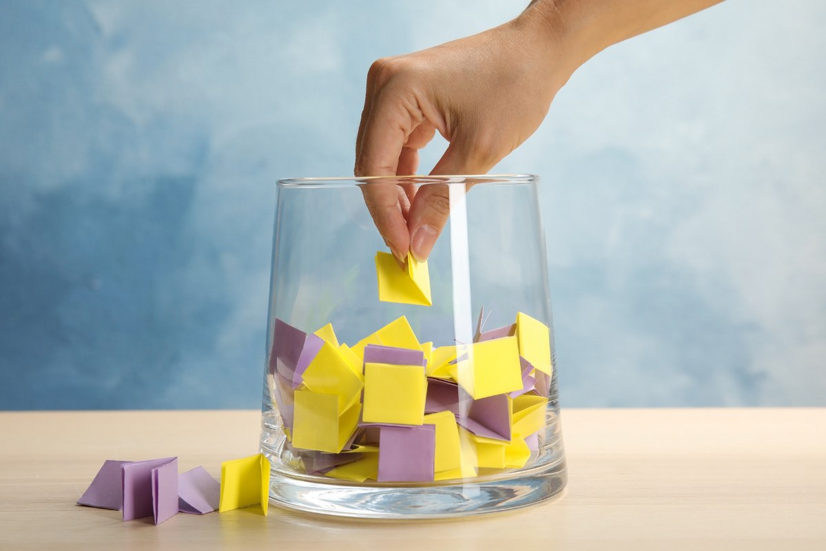 Woman Taking Paper Piece from Glass Vase on Table.