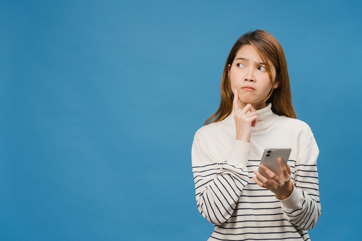 Woman is wondering while holding her cell phone.