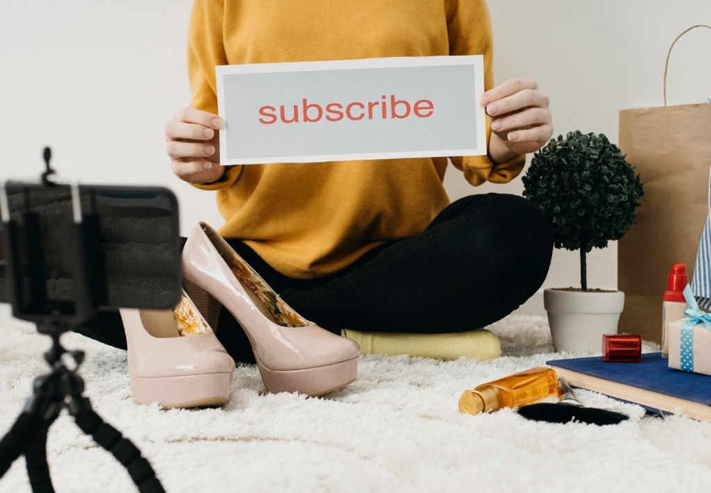 A female fashion blogger asking her viewers to subscribe.
