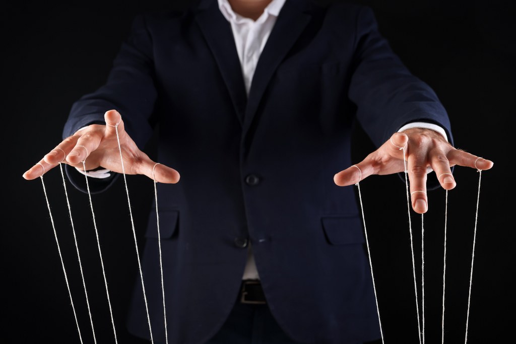 Man in Suit Pulling Strings of Puppet on Black Background, Closeup.