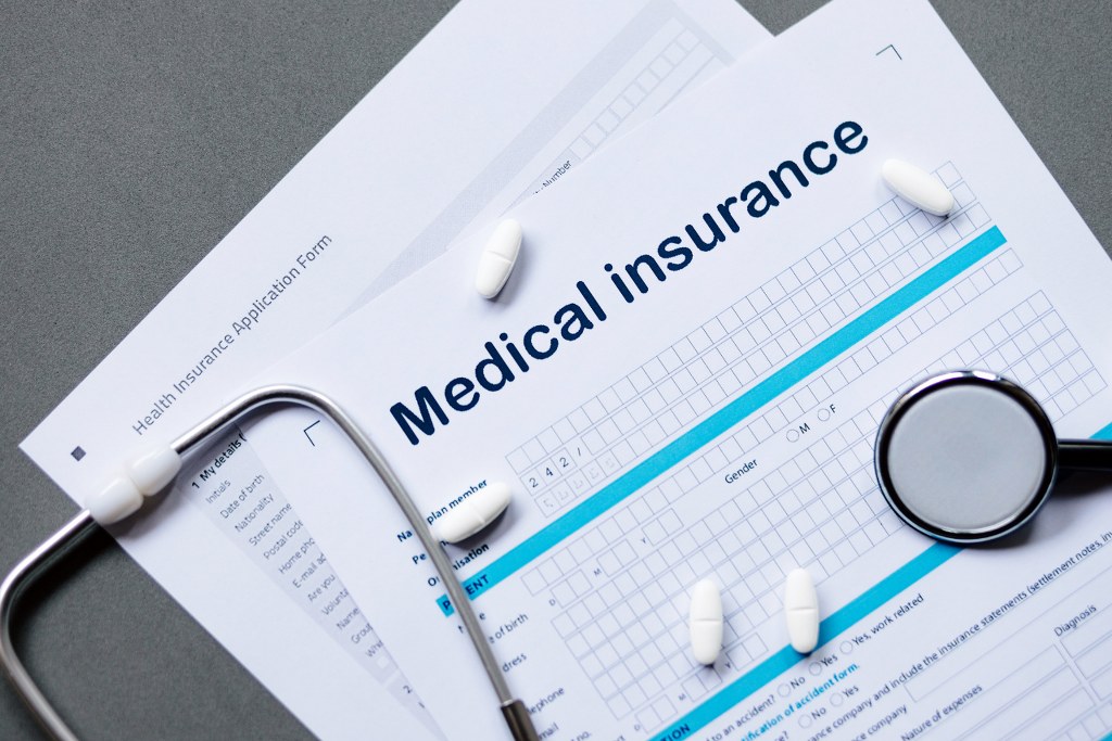 Medical Insurance papers, stethoscope and pills on table.