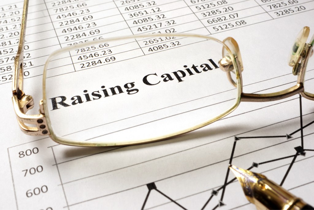 Raising capital writing on paper with glasses on table.