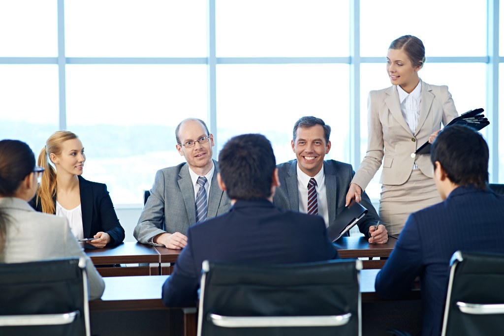 Shareholders having a meeting, a secretary giving out folders with documents.