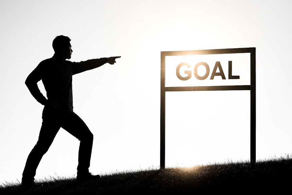 A man pointing at a 'GOAL' sign.