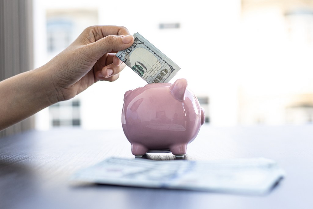 Businessman's hand putting dollar bill inside piggy bank.