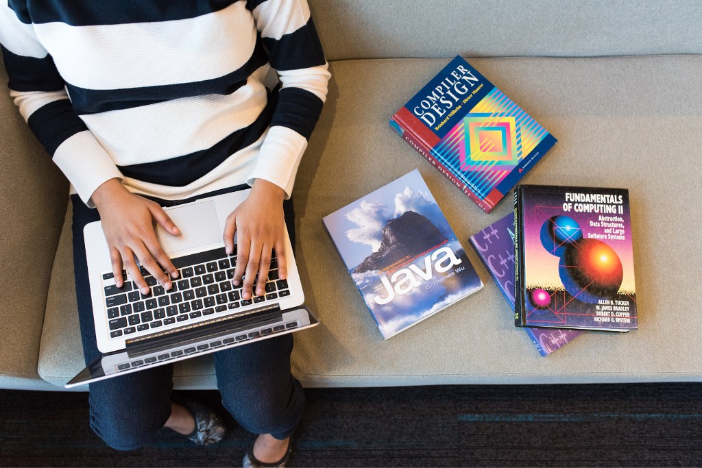Person with laptop and books related to coding.