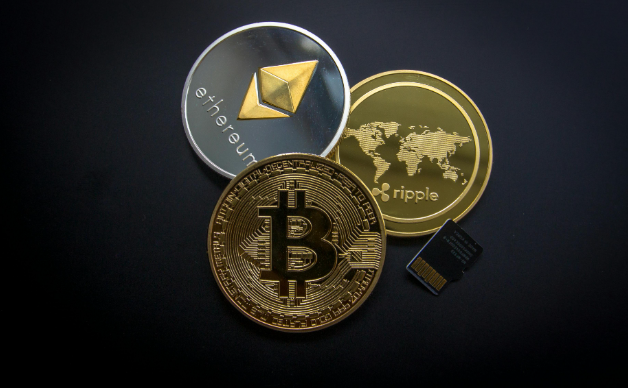 Close-up photo of three cryptocurrency coins—Bitcoin in gold, Ethereum in silver, and Ripple in gold—placed on a black background next to a small memory card