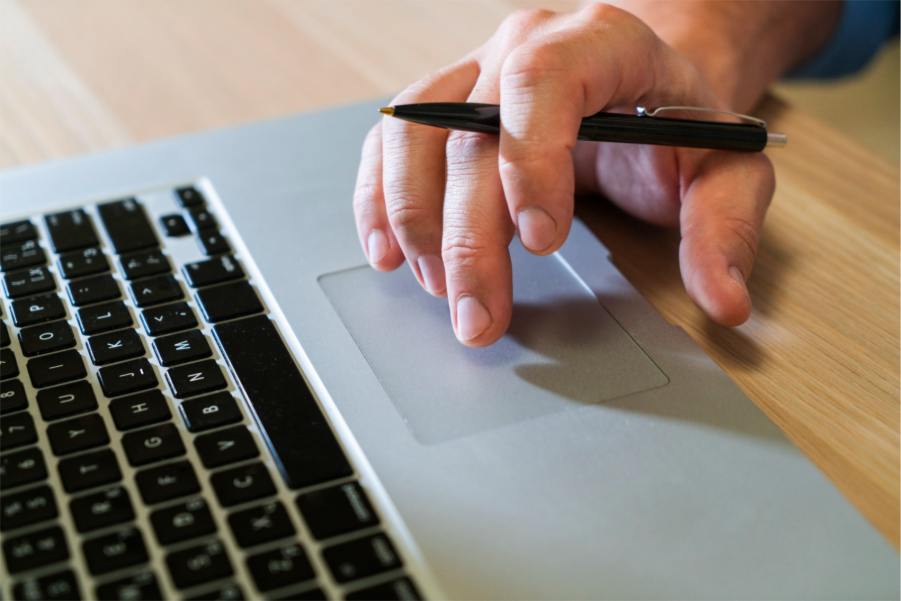Close-up of a person’s hand holding a pen while using the touchpad on a laptop.