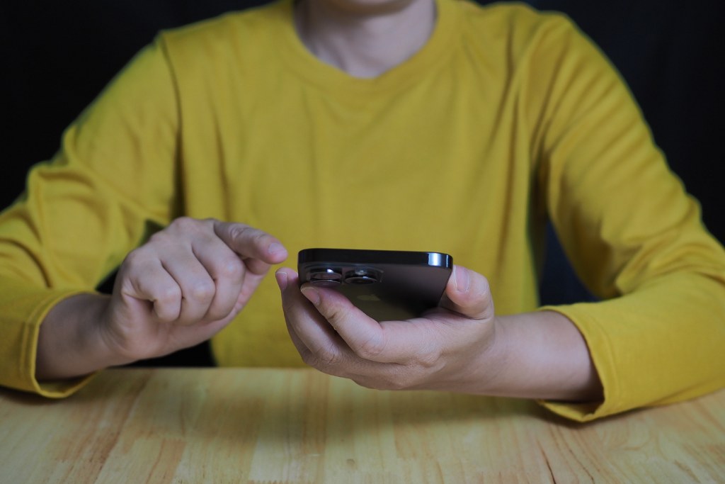 User Interacting with Smartphone on Wooden Table.