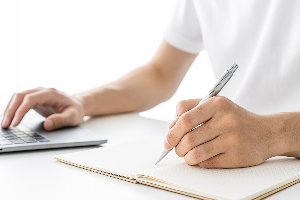 A man writing while using a laptop.