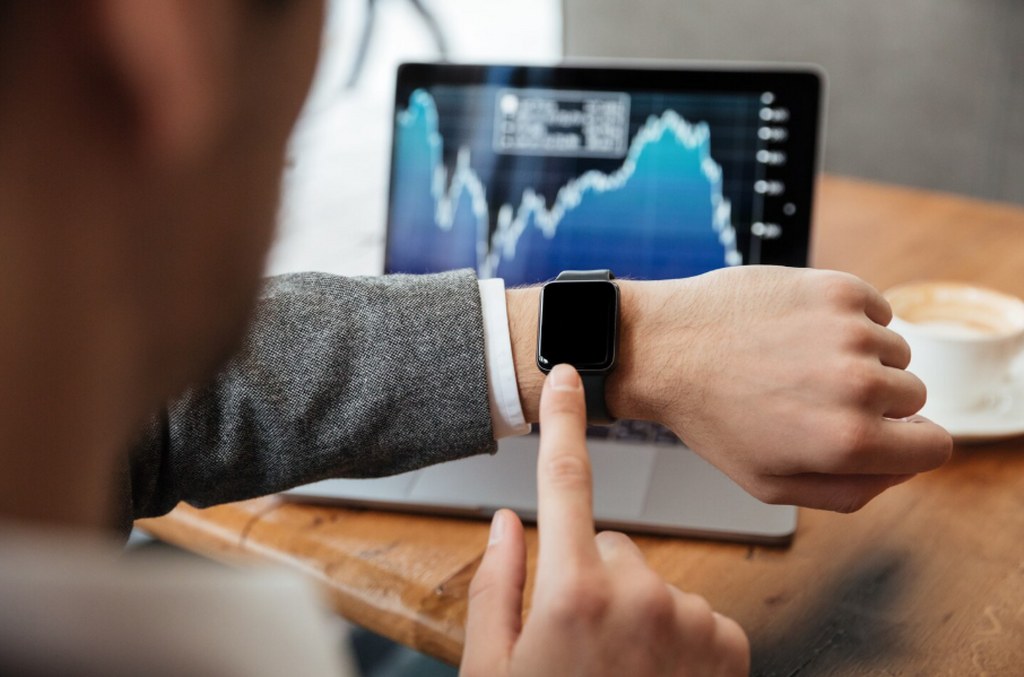 A site reliability engineer looking at his watch with a screen showing an uptime graph in the background.