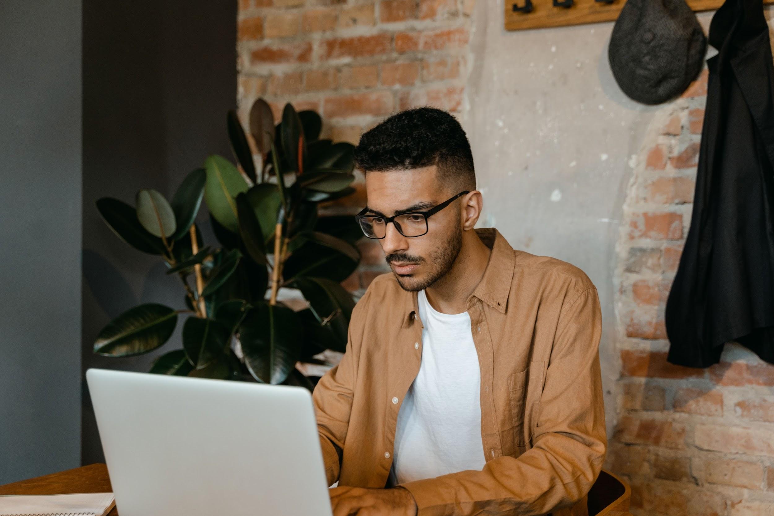 man in brown dress shirt typing on a macbook pro