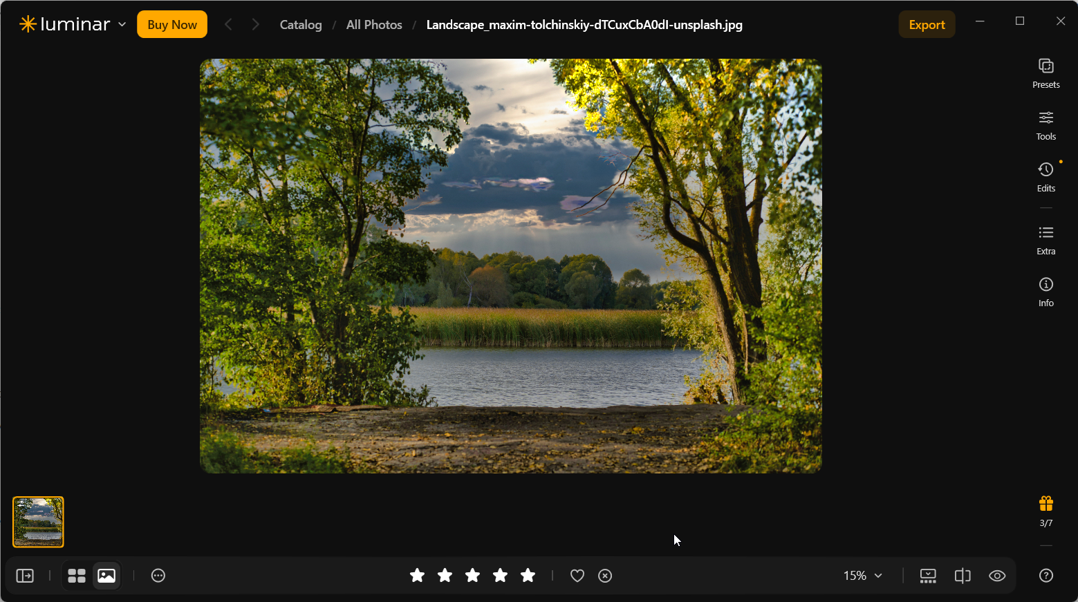 Luminar Neo lake landscape with a dramatic dark-cloud replacement sky, brightly lit yellow-green trees, and calm reflective water after Sky AI refinement.